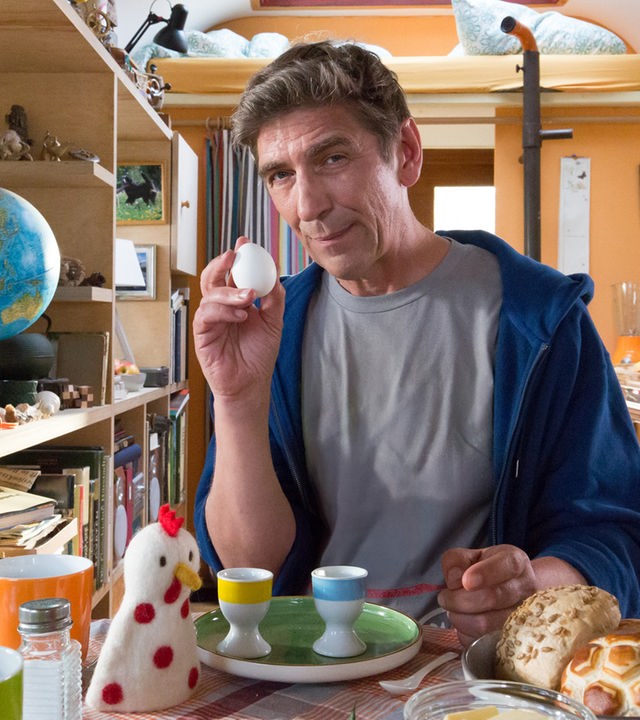 Fritz Fuchs steht im Bauwagen und hält ein rohes Ei hoch.