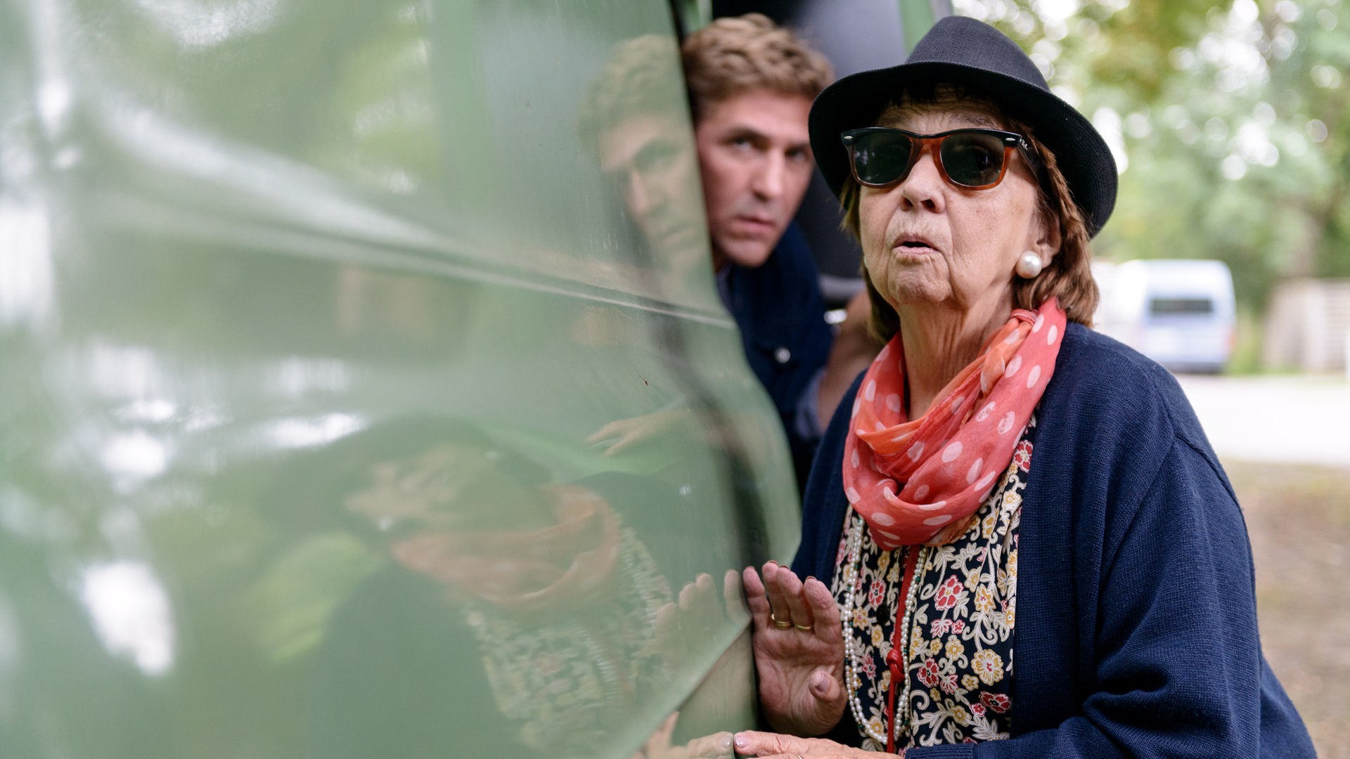 Fritz' Oma Ilse steht an einem Lieferwagen und beobachtet etwas - im Hintergrund ist Fritz zu sehen.