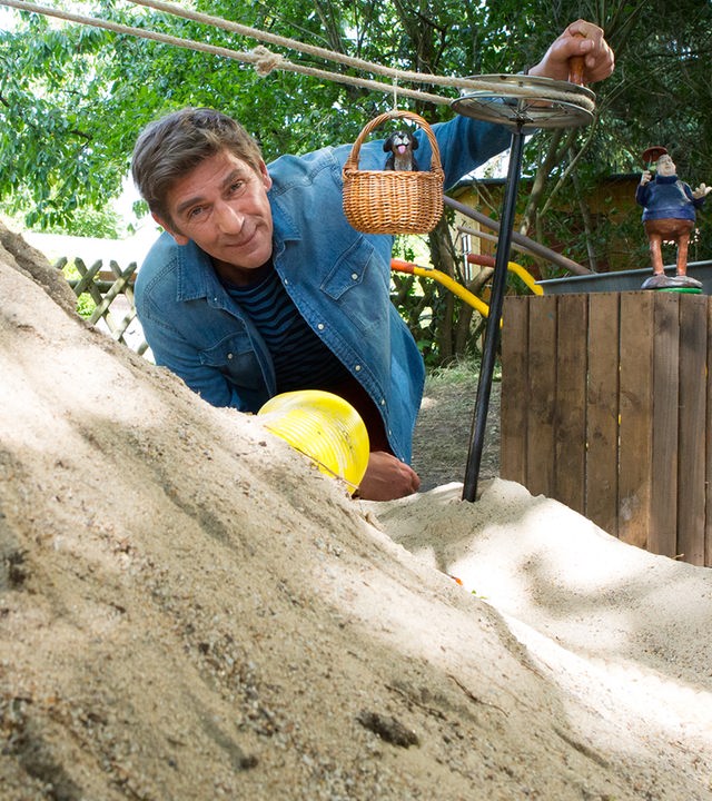 Fritz kniet vor einer selbstgebauten Seilbahn die auf einem Sandhügel steht