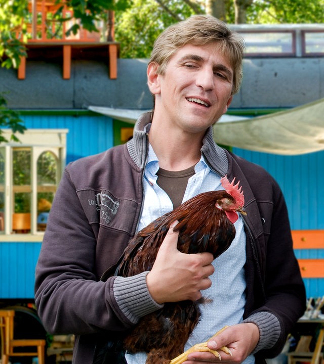 Fritz steht mit einem Huhn auf dem Arm vor dem Bauwagen