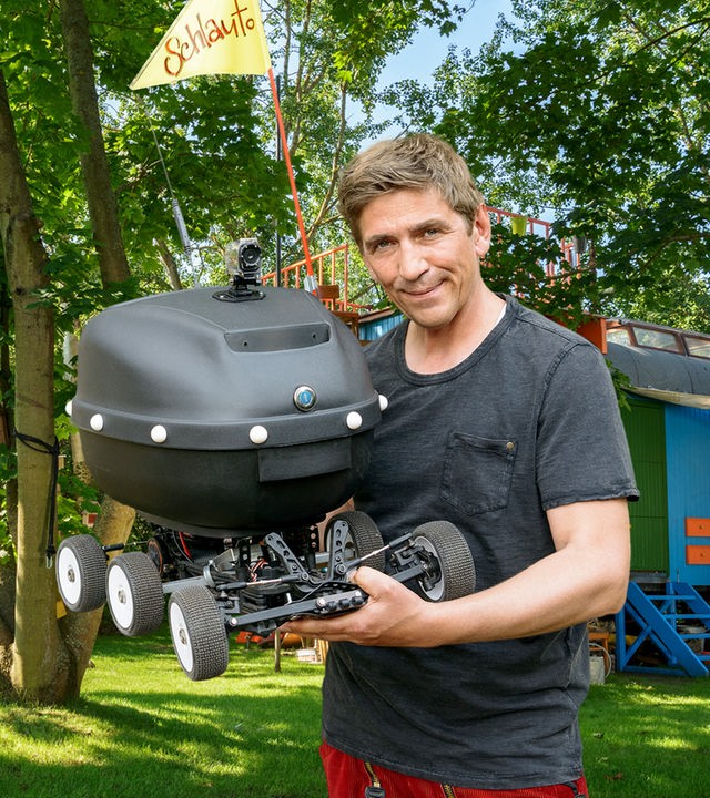 Fritz steht mit seinem selbstgebauten "Schlauto" vor dem Bauwagen