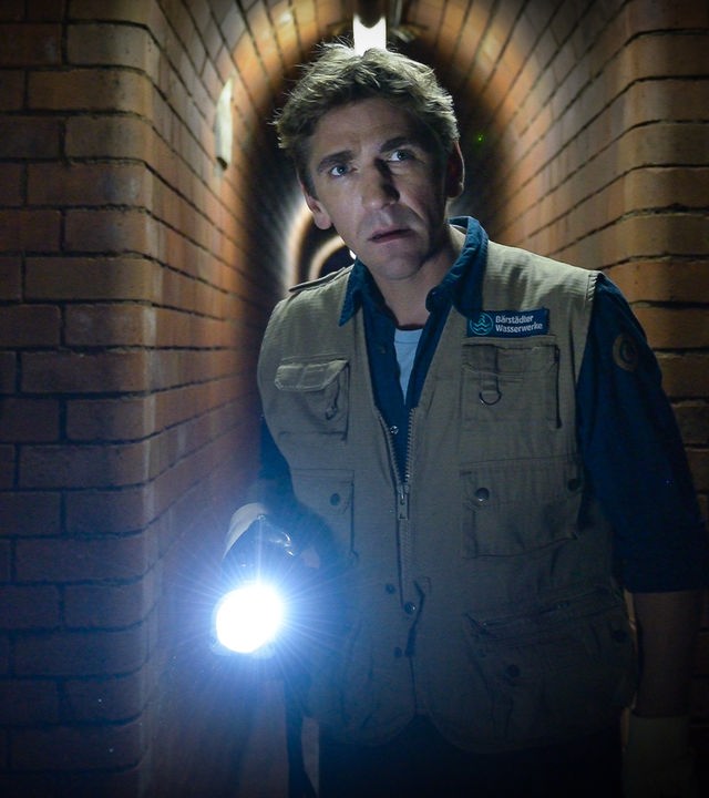 Fritz erkundet mit einer Taschenlampe in der Hand die Kanalisation