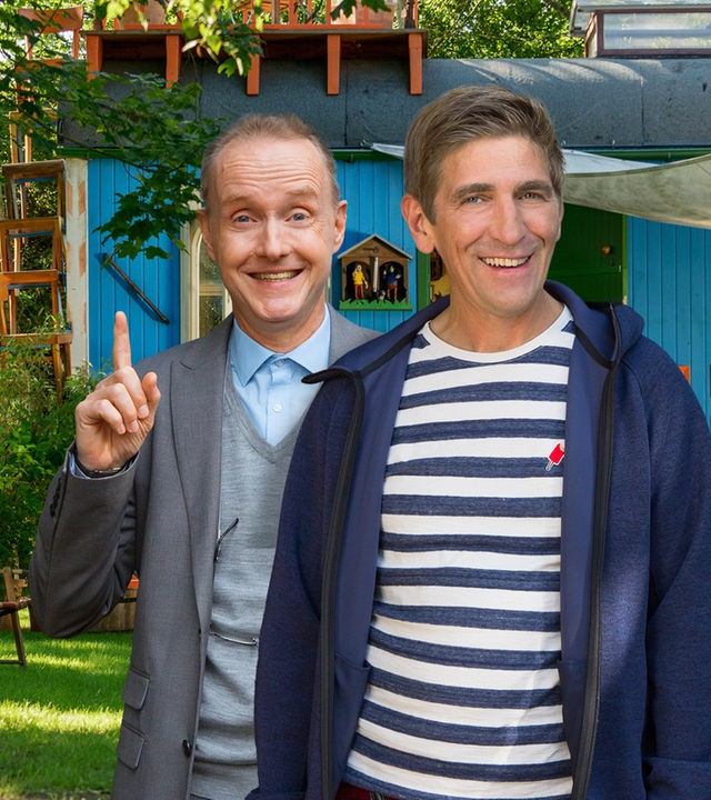 Fritz und Kluthe stehen vor dem Bauwagen und lachen in die Kamera