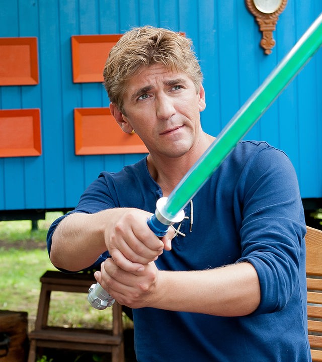 Fritz sitzt vor dem Bauwagen und hat ein Laserschwert in den Händen