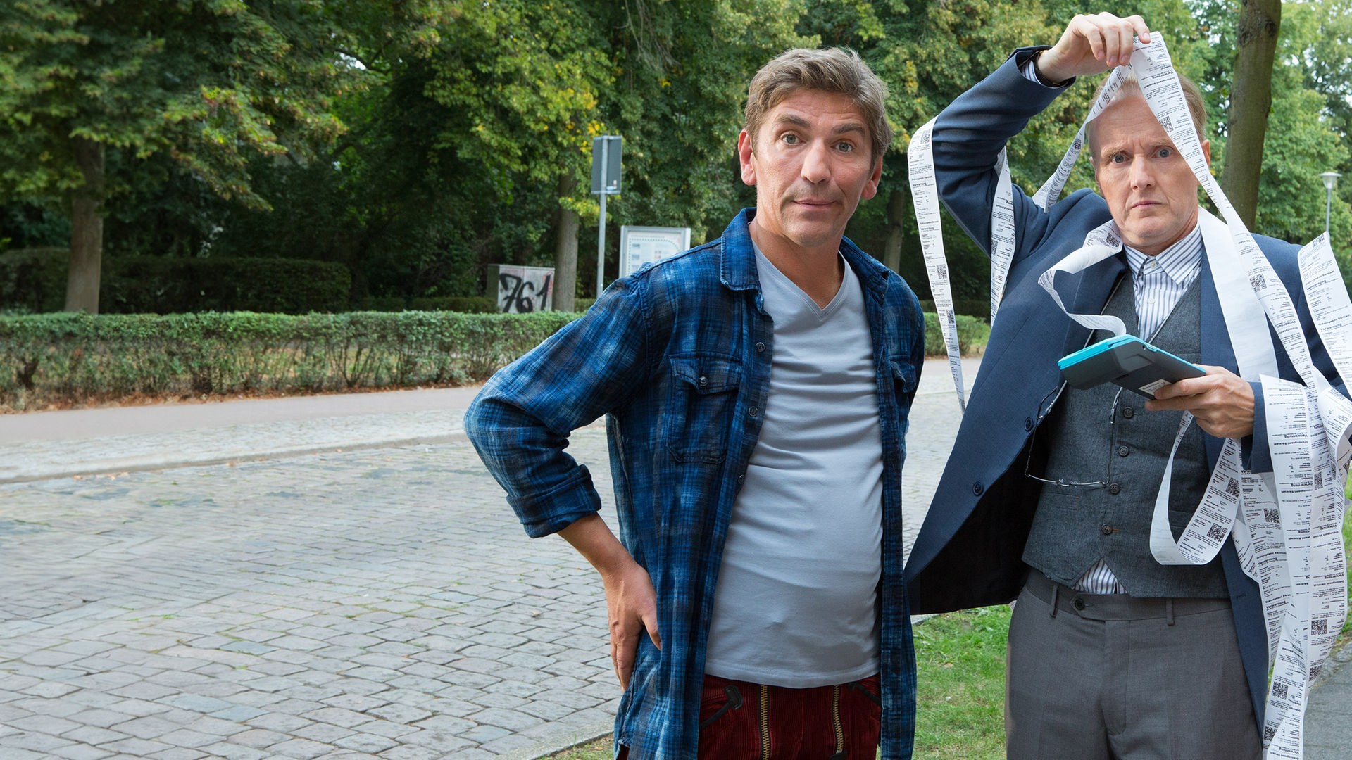 Fritz und Kluthe stehen an einer Straße - Klutze hat sich in einen langen Kassenzettel verheddert