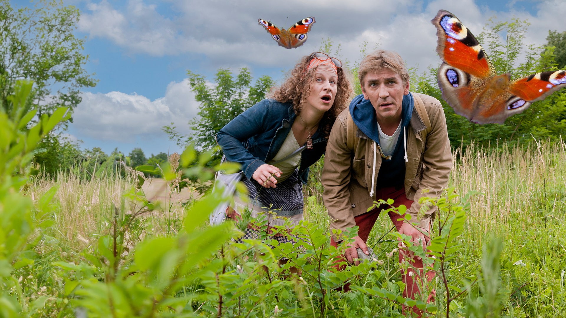 Fritz beobachtet zusammen mit einer Frau einen Schmetterling, der über eine Wiese fliegt