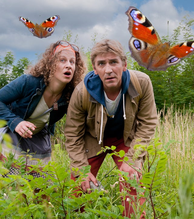Fritz beobachtet zusammen mit einer Frau einen Schmetterling, der über eine Wiese fliegt