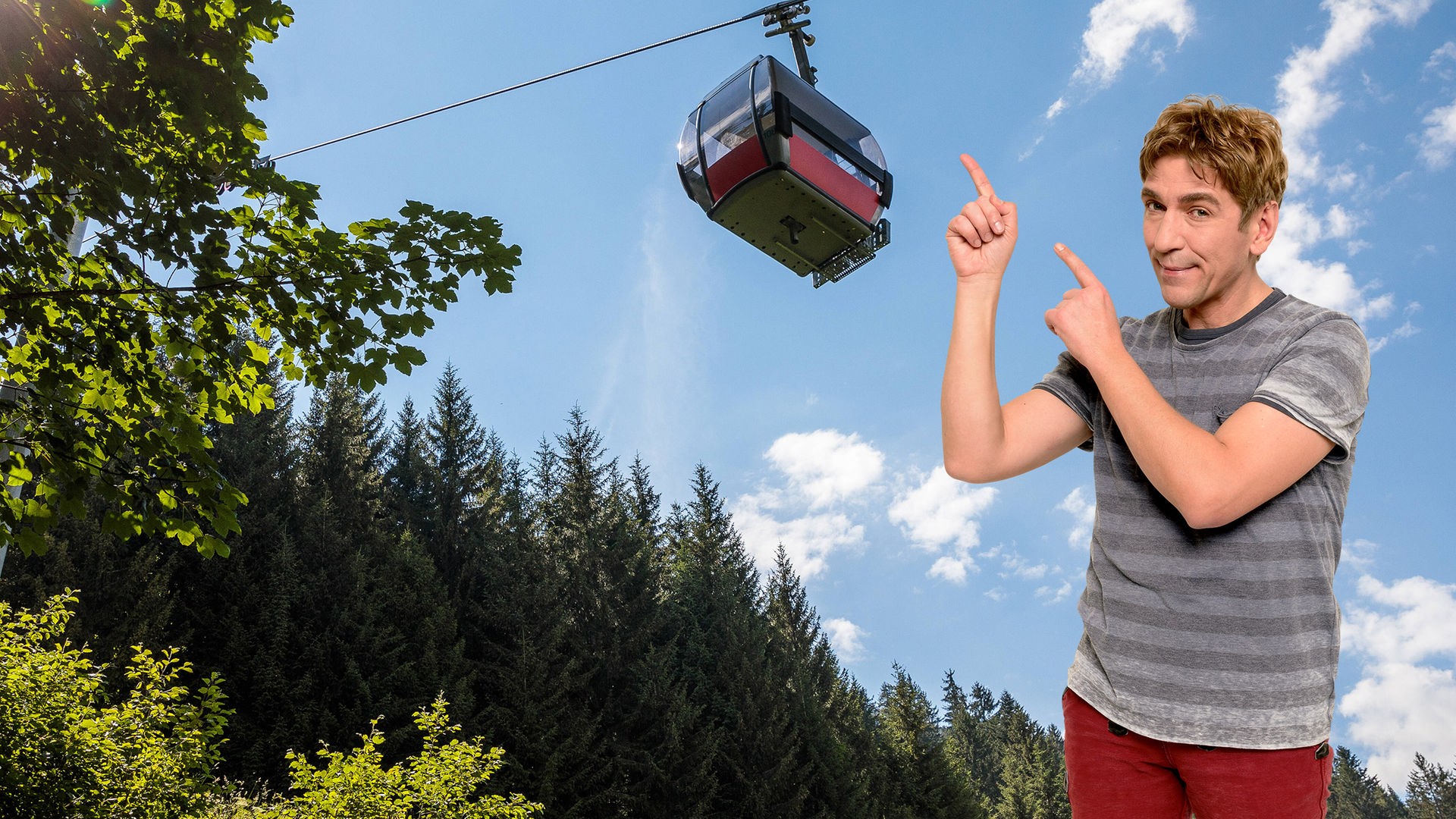 Fritz zeigt mit dem Finger auf eine Seilbahn, die über ihm schwebt