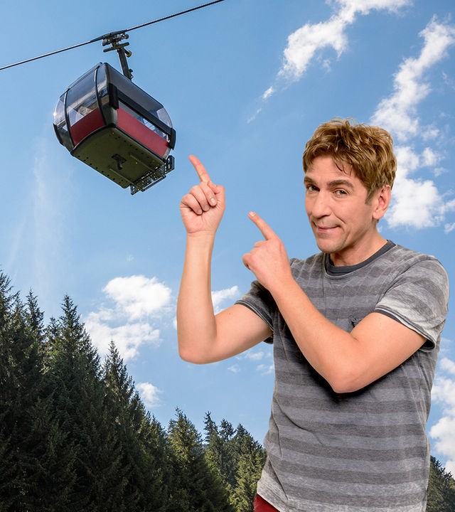 Fritz zeigt mit dem Finger auf eine Seilbahn, die über ihm schwebt