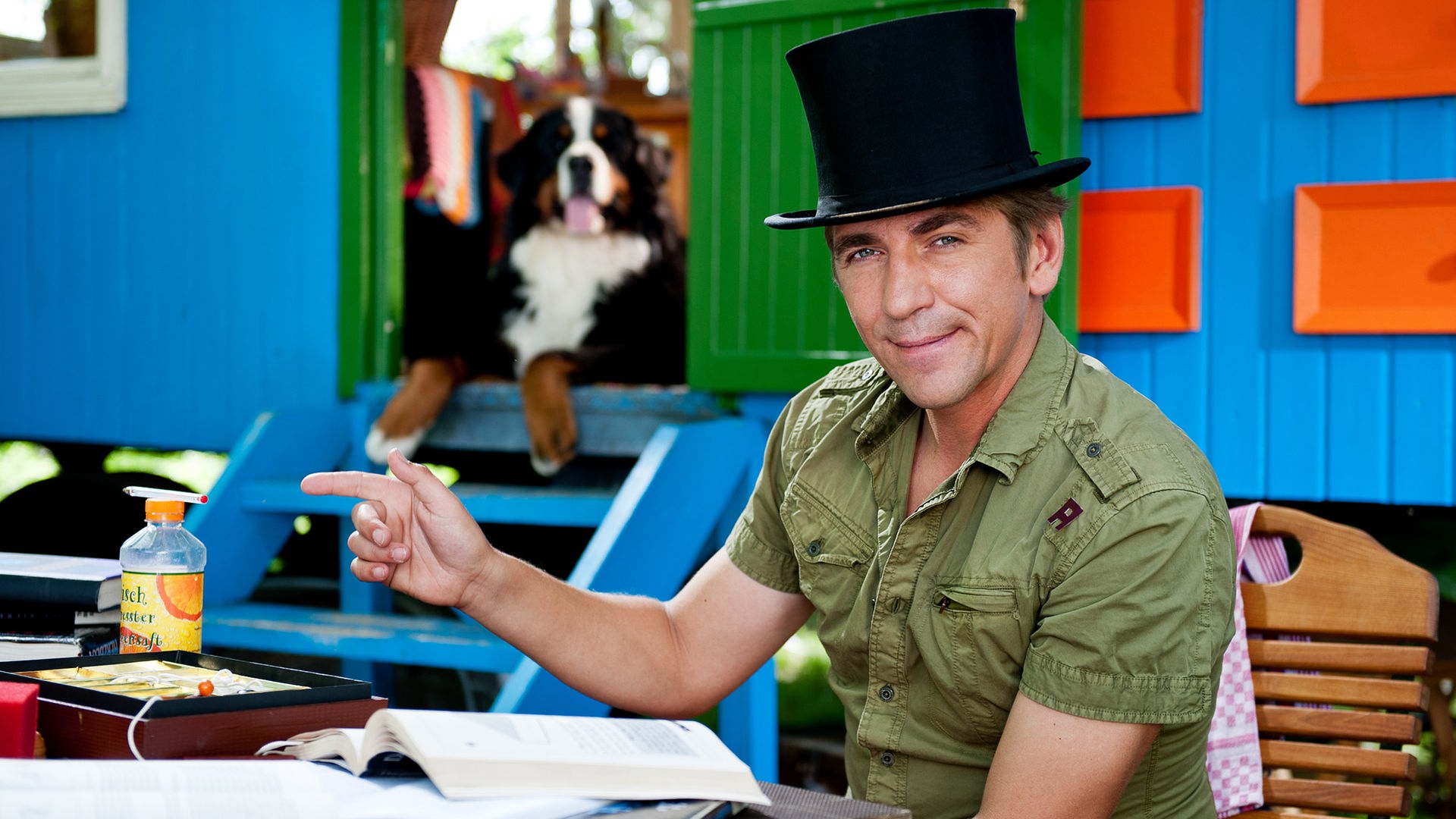 Fritz sitzt vor dem Bauwagen und hat einen schwarzen Zauber-Zylinder auf dem Kopf