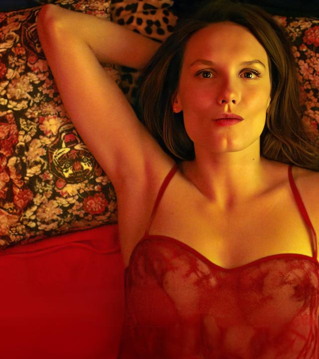  Emma (Ana Girardot) liegt auf einem Bett, der Kopf ruht auf einem geblümten Kissen mit Tigerköpfen.