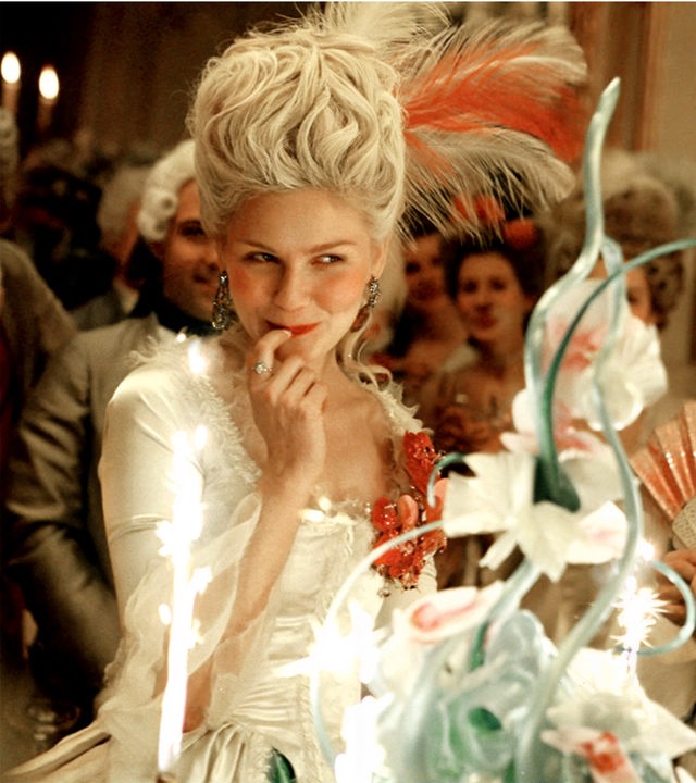 Marie Antoinette (Kirsten Dunst) grinst verschmitzt und fasst sich mit dem rechten Zeigefinger an die Lippe
