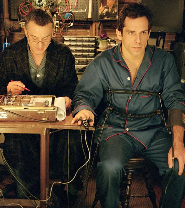 In einem kleinen, holzvertäfelten Raum sitzen Greg Focker (Ben Stiller) und Jack Byrnes (Robert De Niro) nebeneinander an einem Tisch an einem Lügendetektor.