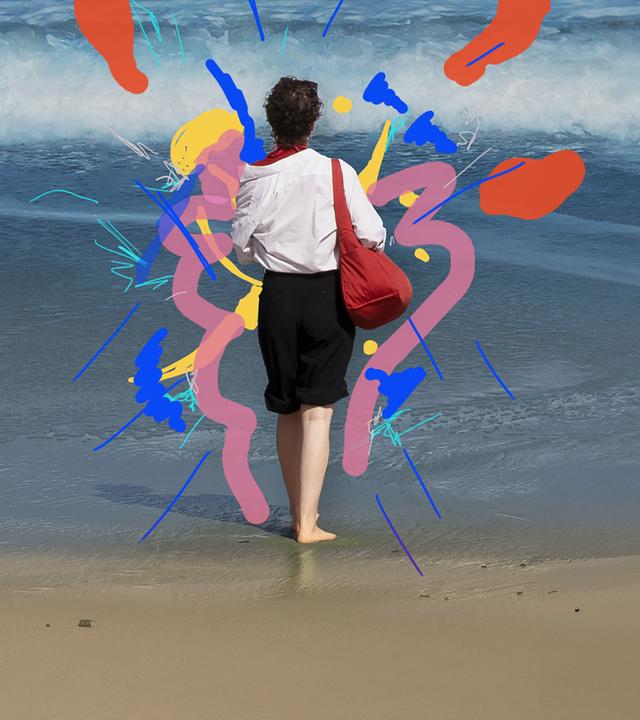 Eine Frau steht am Strand und blickt aufs Meer.