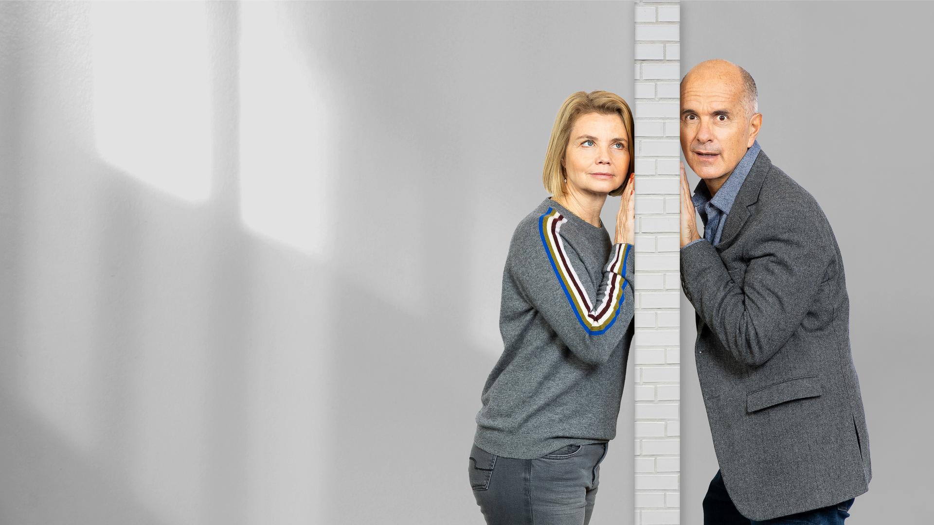 Anne (Annette Frier) und Erik (Christoph Maria Herbst) stehen auf der jeweils anderen Seite einer Wand und halten ihr Ohr gegen diese.