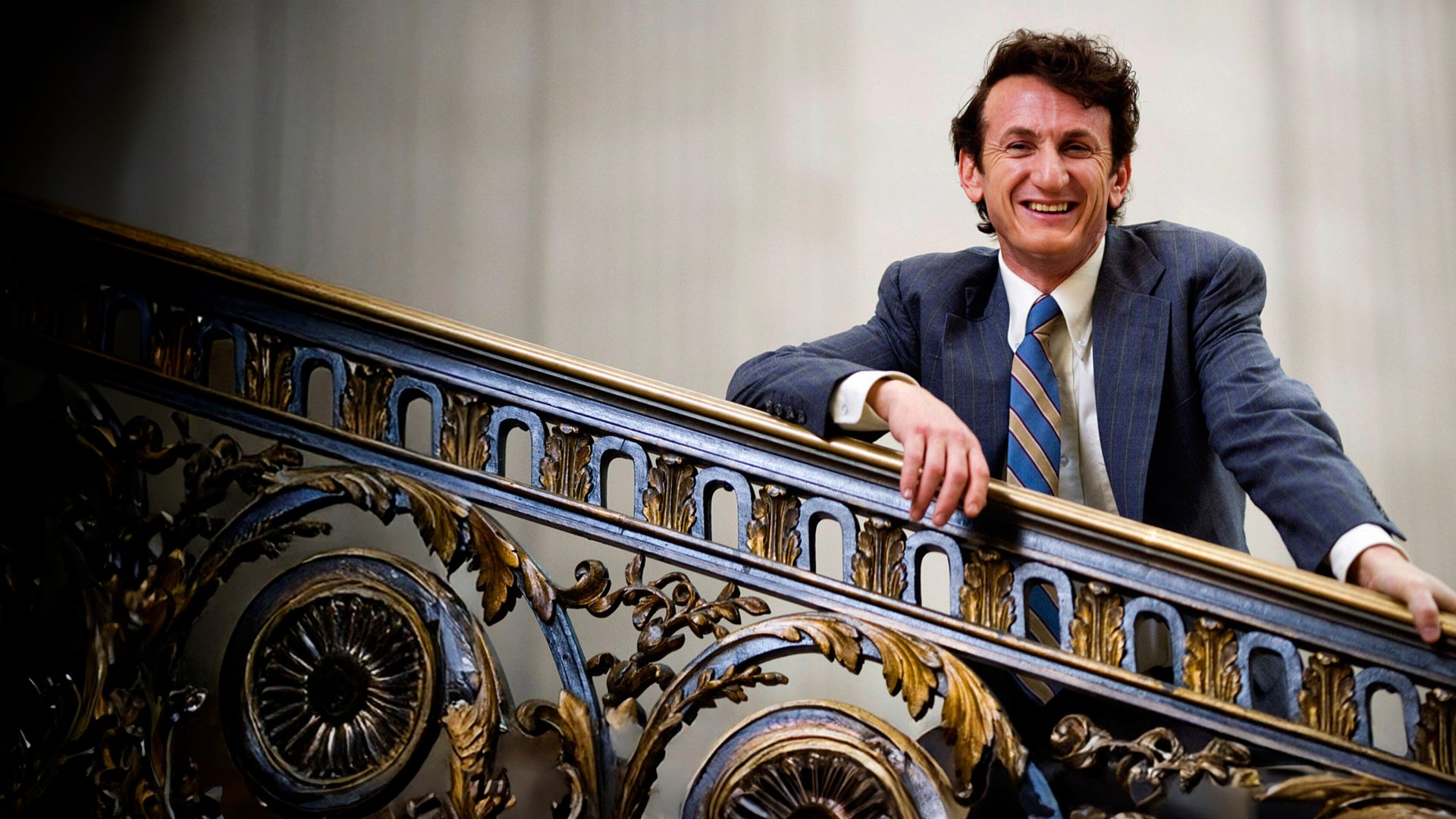 Harvey Milk (Sean Penn) steht auf einer Treppe, lehnt lässig gegen das Gelender und lacht in die Kamera