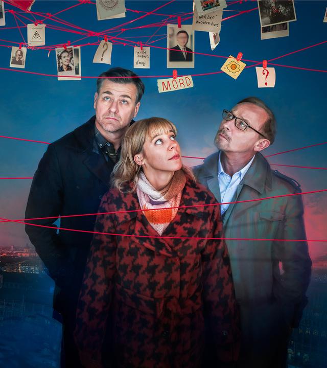 Harald Neuhauser (Marcus Mittermeier; l.); Angelika Flierl (Bernadette Heerwagen; 2.v.l.) und Ludwig Schaller (Alexander Held; r.) begutachten die Umgebung. Am oberen Bildrand hängen rote Fäden an denen Zettel und Fotos angeheftet sind. Im Hintergrund ist München bei Dämmerung zu sehen.