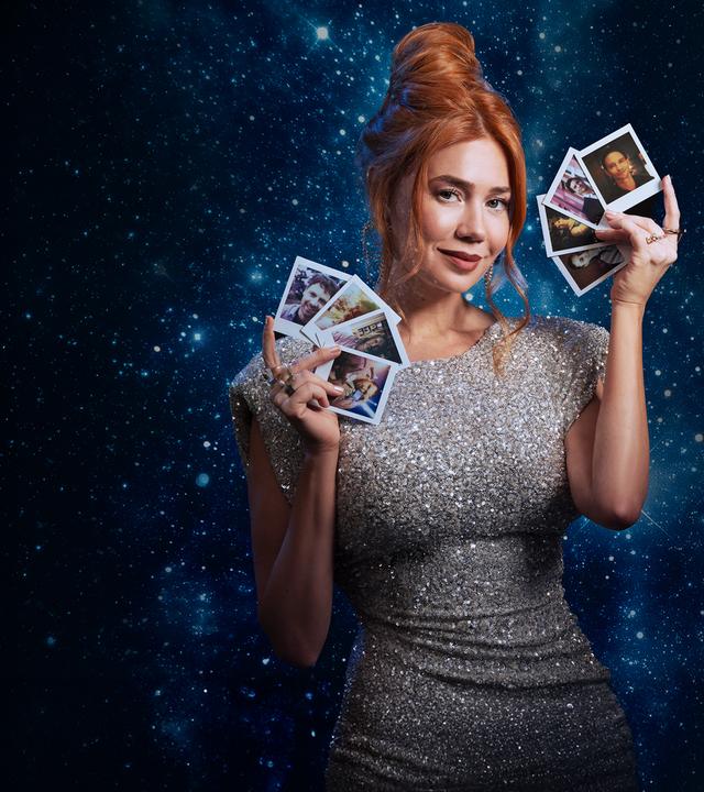 Ivy (Palina Rojinski) steht in einem langen roten Kleid vor einem großen roten Samtherz in dem einige Pfeile stecken. Sie hält einen Pfeil in ihren Händen.