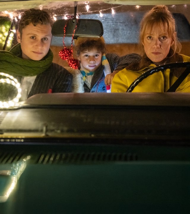 "Nelly und das Weihnachtswunder": Sonny (Rafael Gareisen), Nick (Joah Lion Goetze) und Nelly (Anna Schudt) sitzen in einem Auto, das mit Lichtergirlanden im Inneren geschmückt ist. Nelly sitzt am Steuer, Sonny sitzt neben ihr, Nick sitzt hinter den beiden und hat einen Arm auf Nellys Rückenlehne gelegt. Alle schauen interessiert nach vorne.