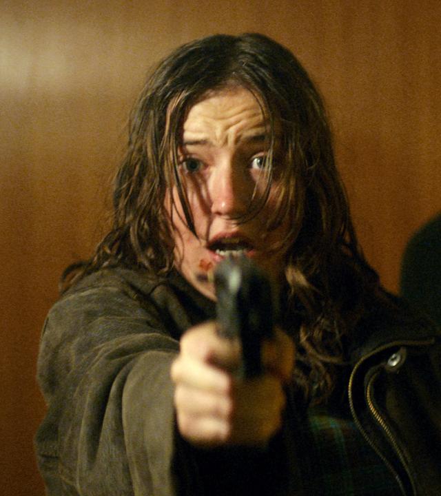 Emma (Fanny Leander Bornedal) hält eine Pistole in der Hand und zielt nach vorne. Sie hat leichte Verletzungen im Gesicht und sieht ängstlich aus. Hinter ihr steht Martin (Nikolaj Coster-Waldau), auch er sieht erschrocken nach vorn.