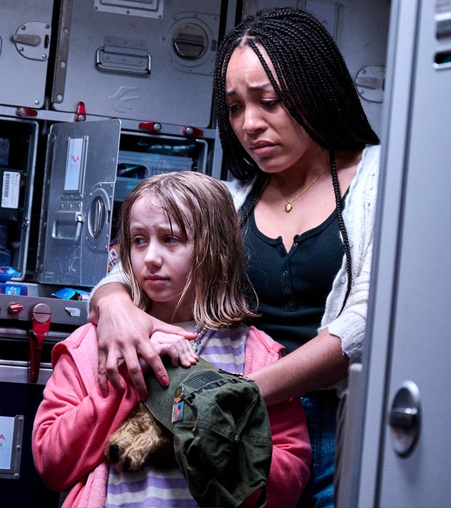 Auch wenn es ihr schwerfällt, versucht Ava (Sophie McIntosh, r.) die kleine Rosa (Grace Nettle, l.) etwas zu trösten. "No Way Up": Ava (Sophie McIntosh) und Rosa (Grace Nettle) stehen vor der Toilette im Flugzeug. Ava hält Rosa im Arm.