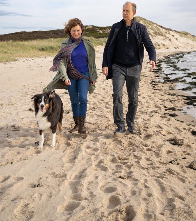 Tabea Krawinkel (Victoria Trauttmansdorff) und Carl Sievers (Peter Heinrich Brix) laufen nebeneinander am Strand entlang. Neben ihnen läuft der Hund Joker.