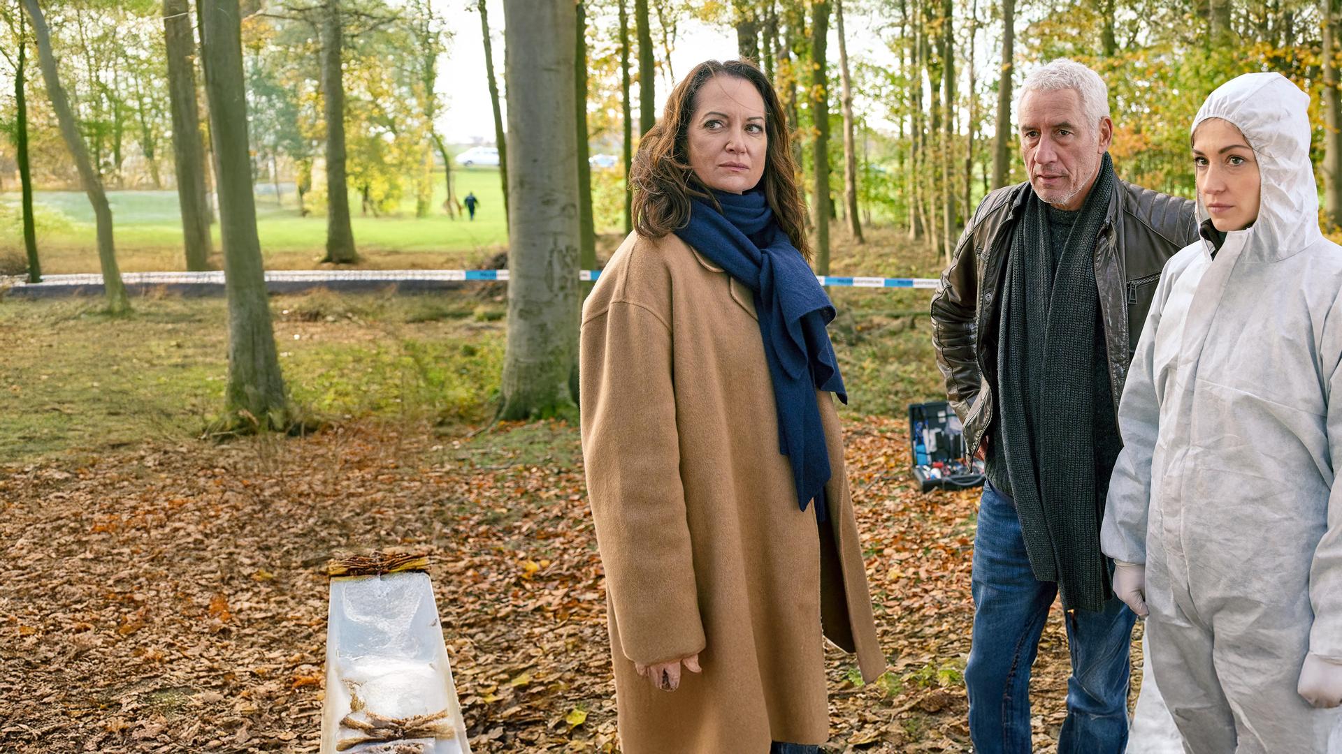 Jana Winter (Natalia Wörner), Matthias Hamm (Ralph Herforth) und Rechtsmedizinerin (Sophia Schubert) stehen an einem Tatort im Wald.