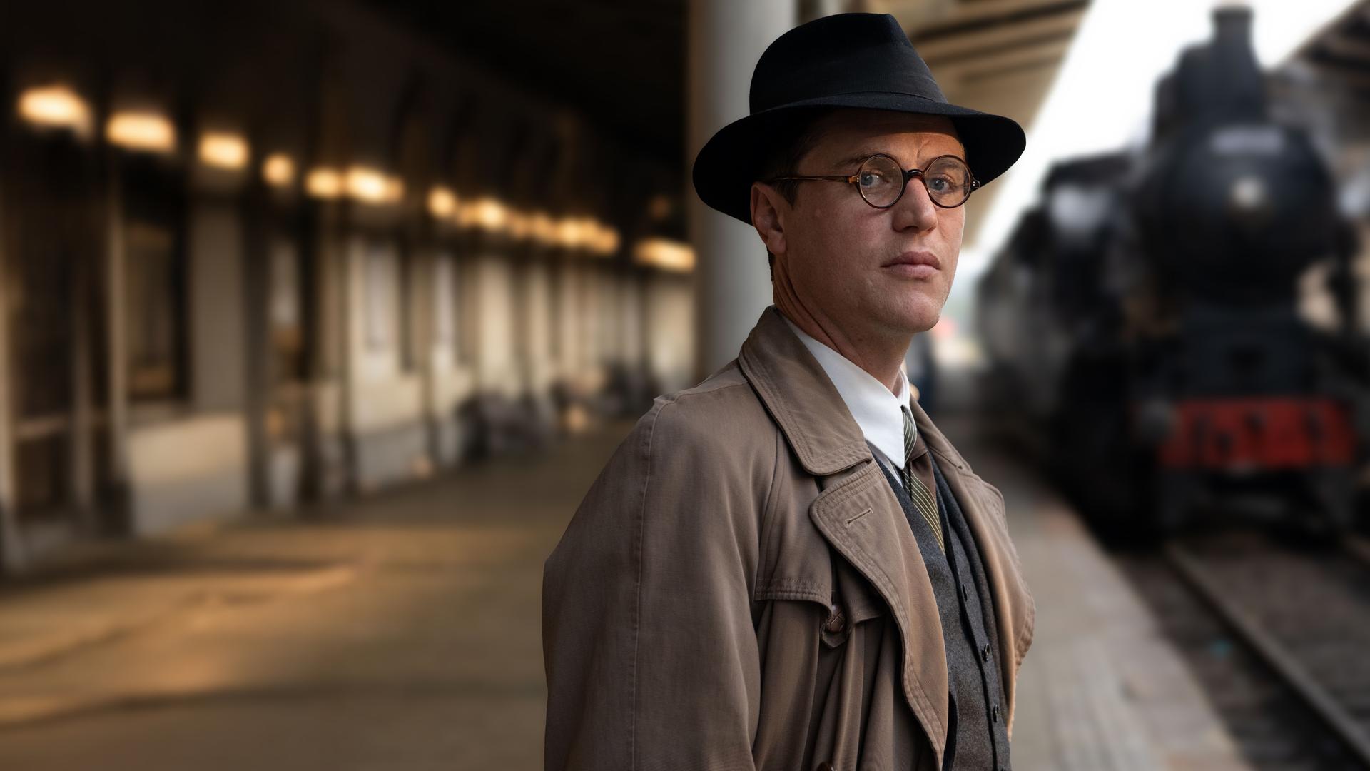 Nicholas (Johnny Flynn) steht im Bahnhof, eine Dampflok fährt ein. Er schaut zur Seite.