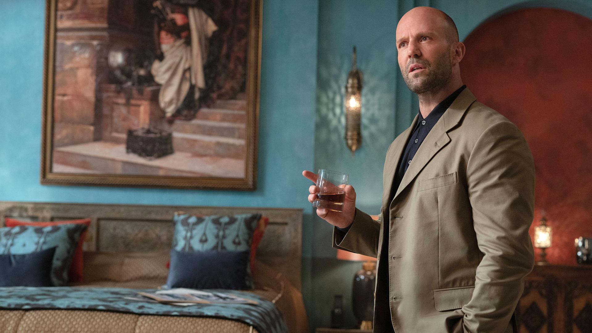 "Operation Fortune": Sarah Fidel (Aubrey Plaza) sitzt an einem Schreibtisch auf dem mehrere Geräte und Bildschirme stehen. Der ganze Raum ist rötlich beleuchtet.