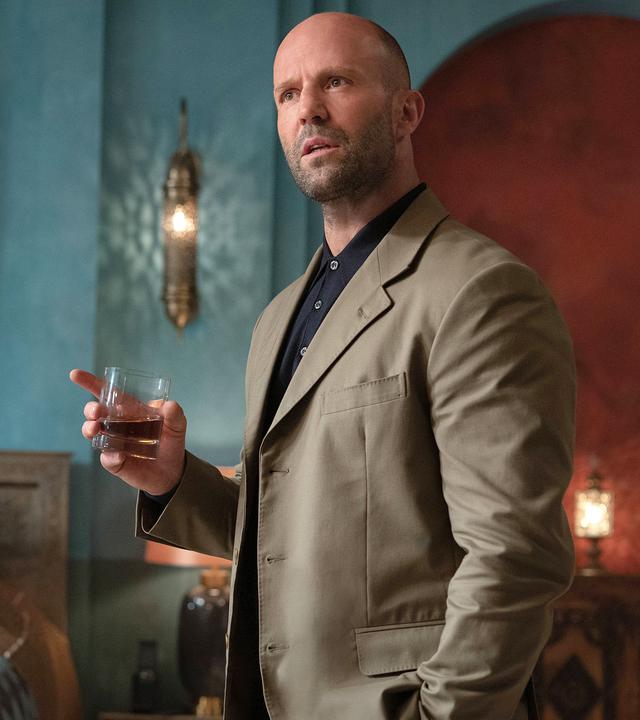 "Operation Fortune": Sarah Fidel (Aubrey Plaza) sitzt an einem Schreibtisch auf dem mehrere Geräte und Bildschirme stehen. Der ganze Raum ist rötlich beleuchtet.