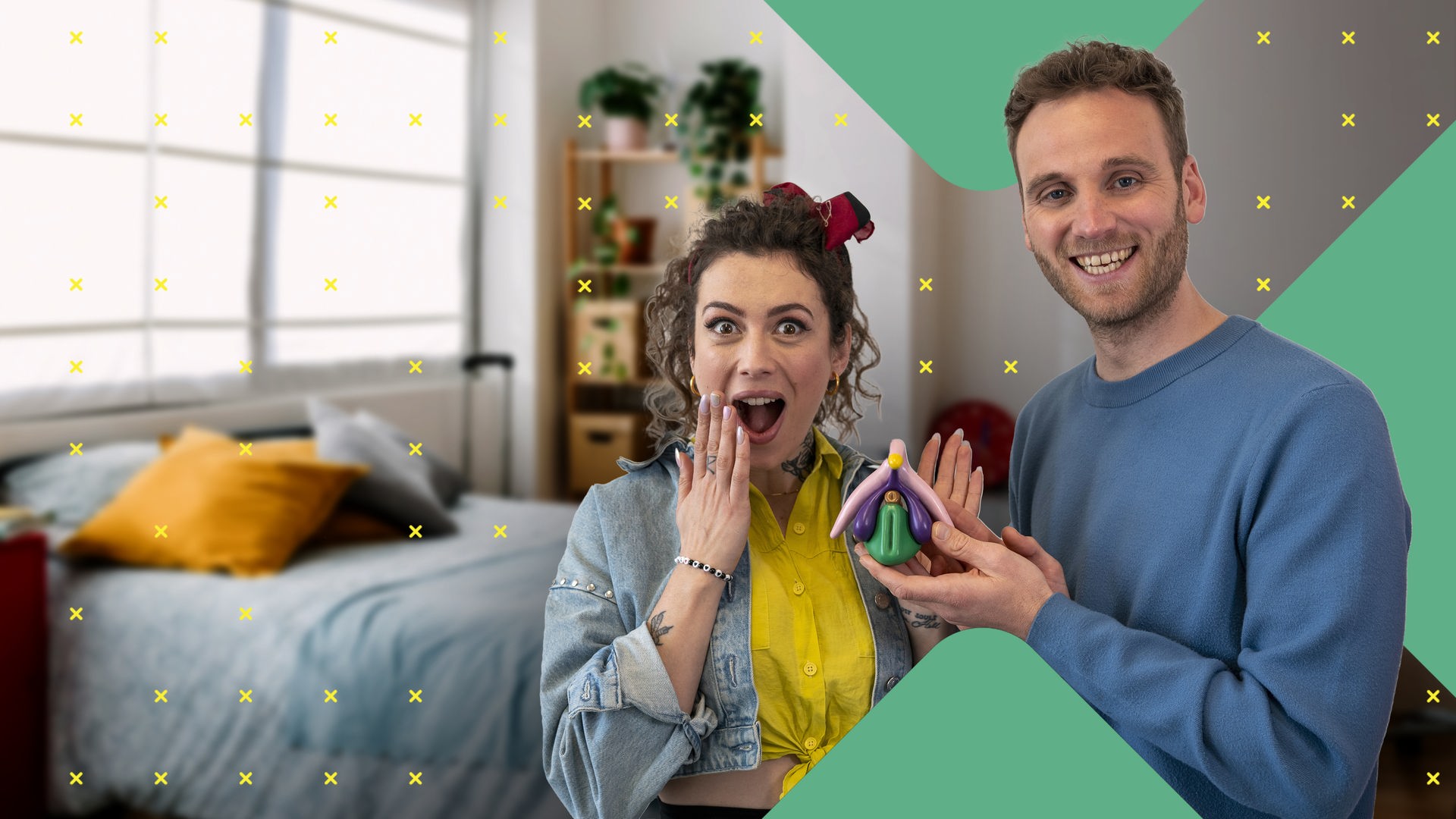 Dr. Leon Windscheid steht im Vordergrund und hält ein farbiges anatomisches Modell einer Klitoris in der Hand. Neben ihm steht Leila Lowfire und blickt überrascht nach vorne. Im Hintergrund befindet sich ein Schlafzimmer mit einem Bett und farbigen Kissen.