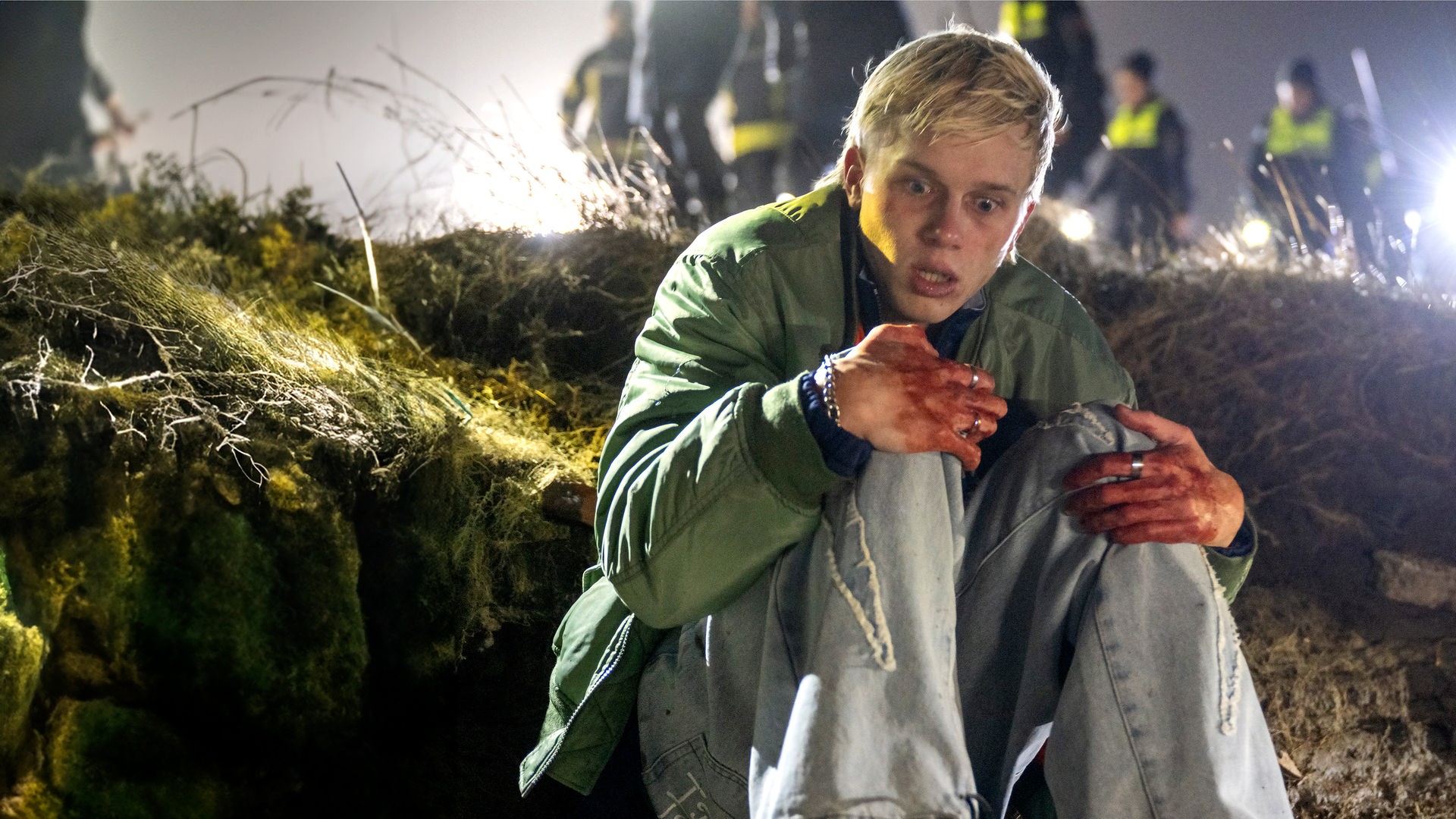 Sichtlich verängstigt und traumatisiert sitzt Marvin Claudius (Noah Kraus) draußen auf dem Boden an einer Düne. Seine Hände sind blutig, er umschlingt seine Knie. Im Hintergrund sieht man verschwommenen mehrere Polizisten (Komparsen) mit Taschenlampen.