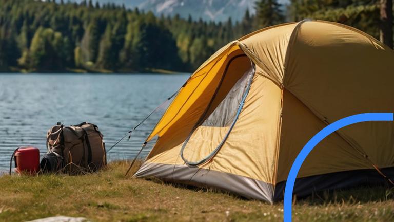 Zelt steht auf einer Wiese vor einem See mit Gebirge im Hintergrund.
