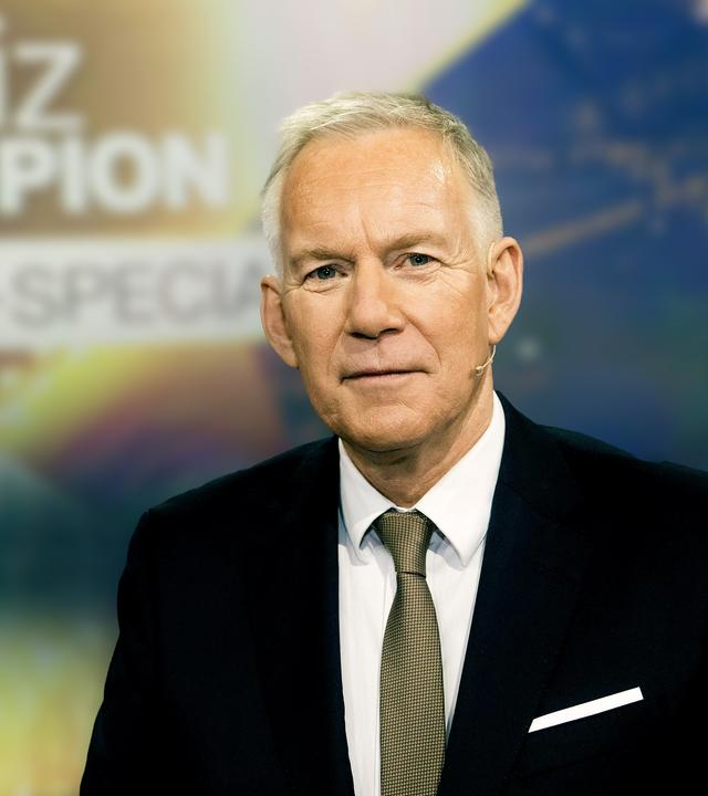 "Der Quiz-Champion - Das 2025-Special" vom 23. Dezember: Johannes B. Kerner steht vor dem Sendungslogo und lächelt in die Kamera.es