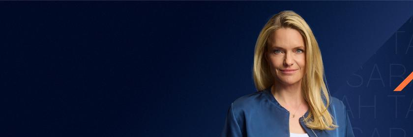 Sarah Tacke schaut selbstbewusst in die Kamera. Hinter ihr ist ein grafischer Hintergrund in blauen Farbklima mit orangenen und magentanen Akzenten zu sehen