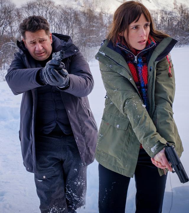 (Clémentine Poidatz) und Andréas Meyer (Laurent Gerra) stehen nebeneinander. Beide haben ihre Waffe in der Hand