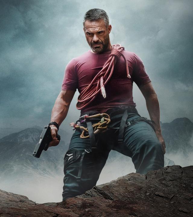 aul Vilar (Philippe Bas) steht auf einem Felsen und schaut in die Tiefe. Er hält eine Pistole in der Hand.