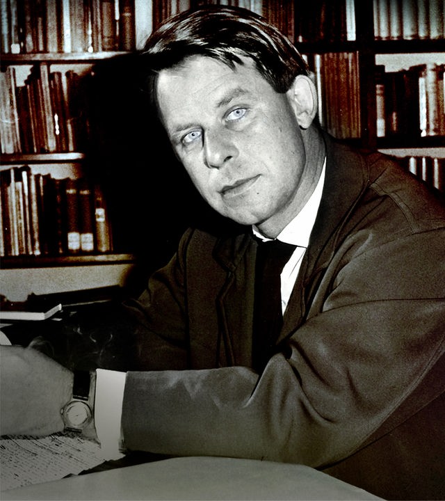 Der junge Siegfried Lenz sitzt vor einer Bücherwand am Schreibtisch (s/w)