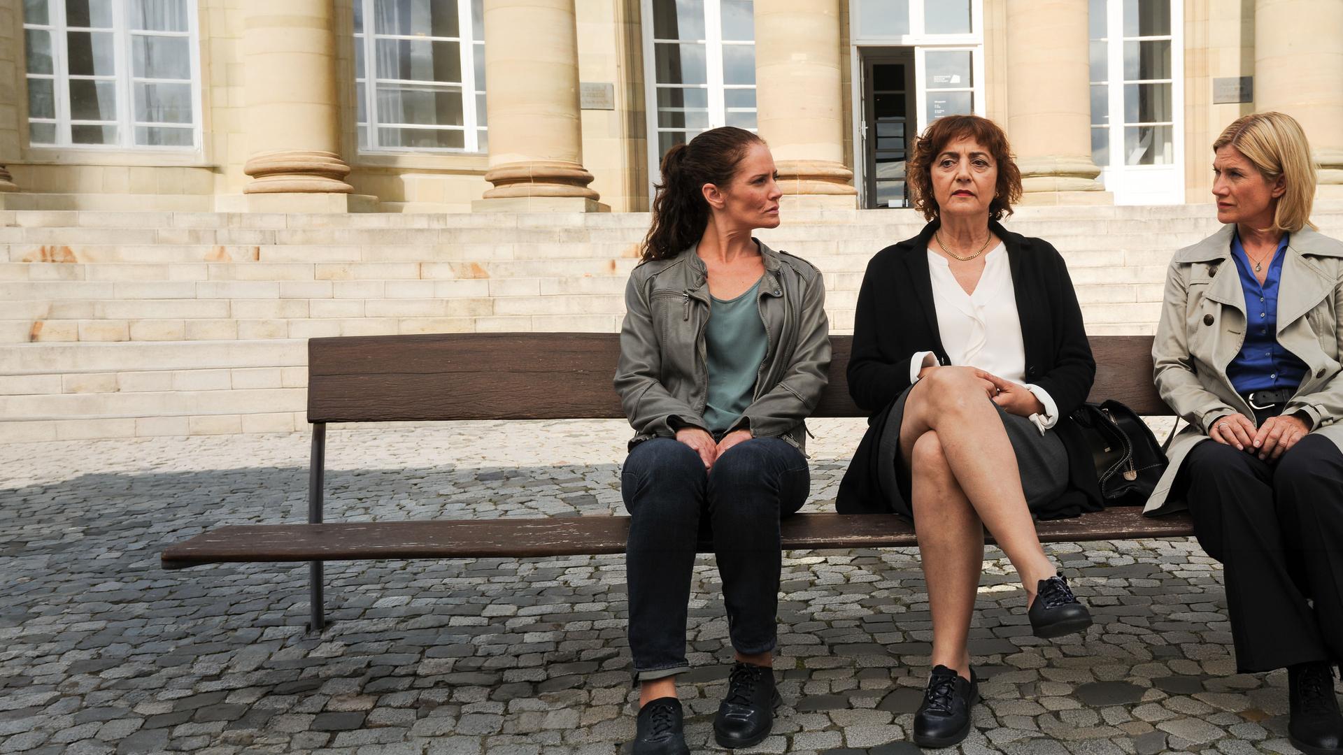 "SOKO Stuttgart - Die Liste": Paola Eisele (Despina Pajanou) sitzt auf einer Bank zwischen Selma Kirsch (Yve Burbach) und Martina Seiffert (Astrid M. Fünderich). Die Kommissarinnen schauen Paola an, diese starrt ins Leere.