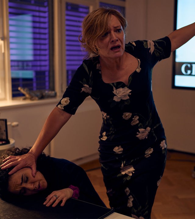 "SOKO Wien - In Schönheit sterben": Ilona Gerber (Marion Mitterhammer) steht hinter Dilaria Yildiz (Mariam Hage) und drückt deren Kopf auf die Schreibtischplatte. Ilona Gerber hat ihren linken Arm ausgestreckt um Schwung zu holen, damit sie Dilaria erschlagen kann.