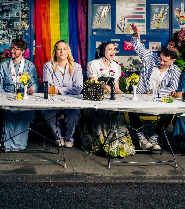 Die sechs Bewohner der Glaubens-WG sitzen vor einem Kiosk und schauen gemeinsam in die Kamera.