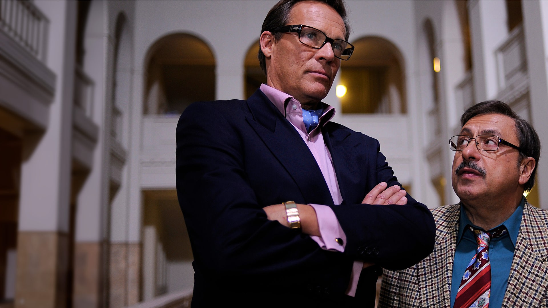 Werner Stankowski (Wolfgang Stumph) steht mit Rene Vonderecken (Christian Tramitz) in der Empfangshalle der Treuhand und schaut skeptisch zu ihm auf. Vonderecken steht mit verschränken Armen neben ihm und schaut in die Ferne.