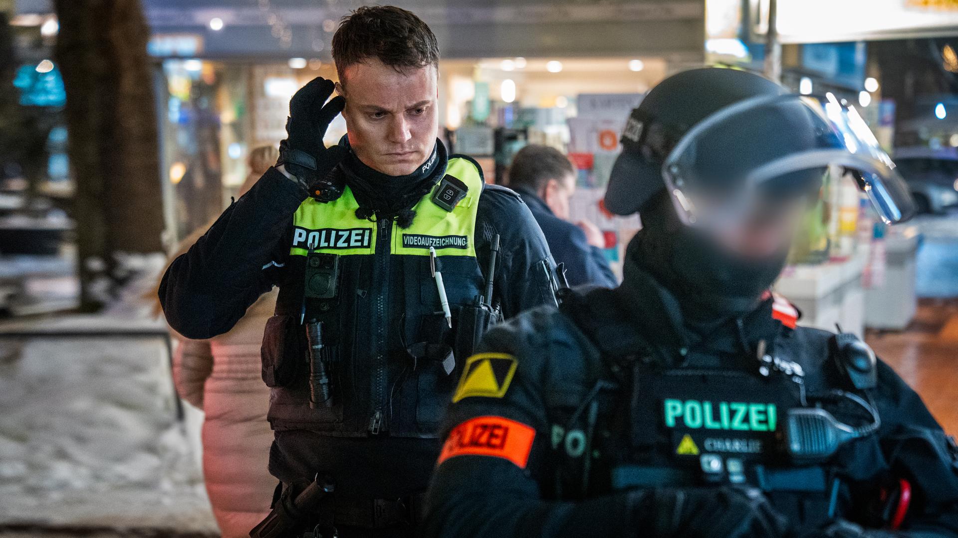 Ein Polizist auf Streife und ein Polizist vom Interventionskommando bei einem Einsatz auf einem Parkplatz bei Nacht. Der Polizist des Einsatzkommandos ist mit Helm und Sicherheitsweste ausgerüstet.