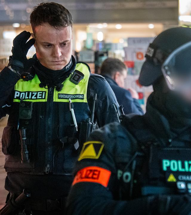 Ein Polizist auf Streife und ein Polizist vom Interventionskommando bei einem Einsatz auf einem Parkplatz bei Nacht. Der Polizist des Einsatzkommandos ist mit Helm und Sicherheitsweste ausgerüstet.
