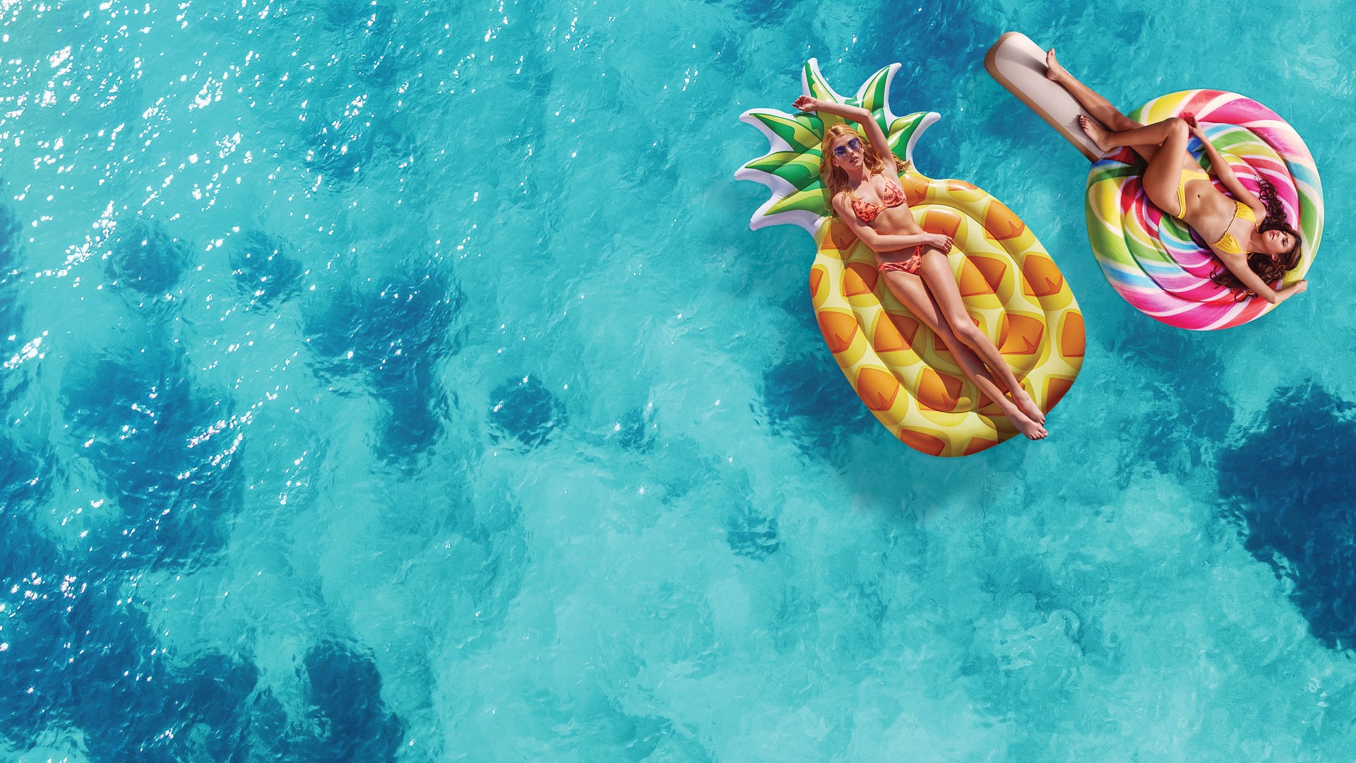 Chloe (Katherine McNamara) (links) und Melanie (Jasmine Sky Sarin) (rechts) liegen auf Luftmatratzen in Form einer Ananass und eines Lolipops auf der Wasseroberfläche.