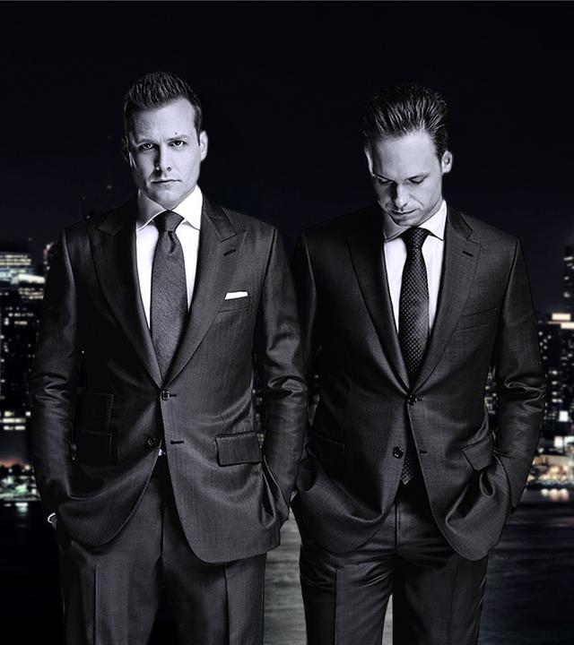 Star-Anwalt Harvey Specter und der clevere Mike Ross stehen nachts in teuren Anzügen vor der New Yorker Skyline.