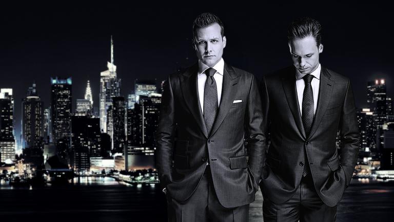 Star-Anwalt Harvey Specter und der clevere Mike Ross stehen nachts in teuren Anzügen vor der New Yorker Skyline.