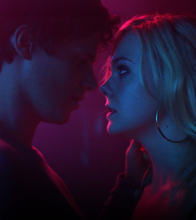 Teen Spirit": Nahaufnahme - Keyan Spears (Ruairi O'Connor) beugt sich mit intensivem Augenkontakt zu der nah vor ihm an einer Wand lehnenden Violet (Elle Fanning) zu einem Kuss vor. Die beiden, die im Profil zu sehen sind, werden von pinkfarbenem Licht angestrahlt.