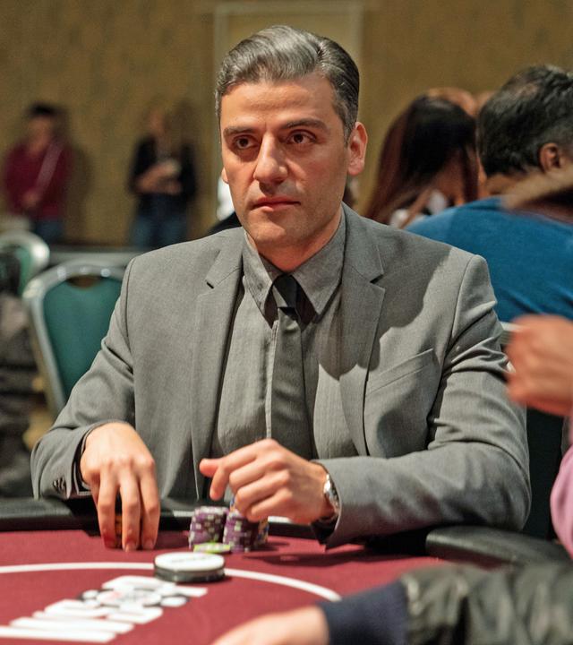 Nahaufnahme: William Tell (Oscar Isaac) sitzt in einem grauen Anzug und Krawatte an einem Pokertisch. Vor ihm liegen zwei Stapel Chips und er schaut konzentriert nach vorn. Um ihn herum sind verschwommen weitere Spieler zu sehen.