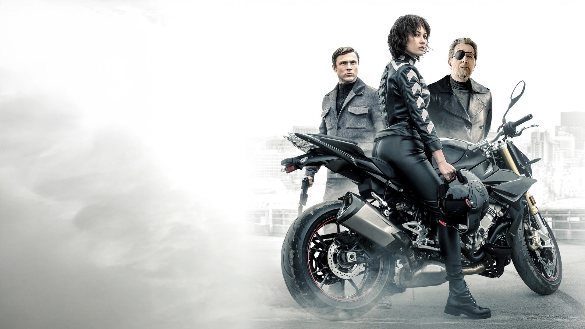 Der Kurier (Olga Kurylenko) sitzt auf einem Motorrad und sieht zur Kamera. Hinter dem Kurier sind Ezekiel Mannings (Gary Oldman) und Agent Bryant (William Moseley) zu sehen.